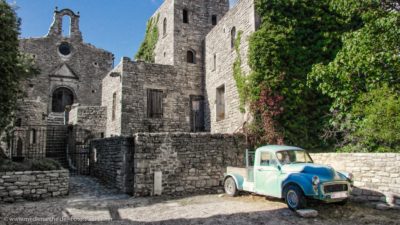 Ein Oldtimer vor einer Burg. Das blaue Auto bildet einen Kontrast zu den grauen Steinmauern der Burg.