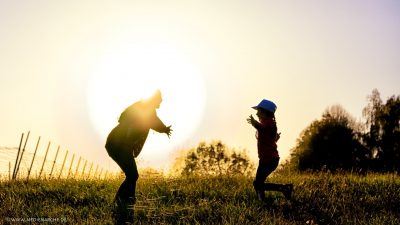 Ein Kind rennt aus dem schattigeren Bereich in die Arme der von der Sonne leuchtenden Mutter.